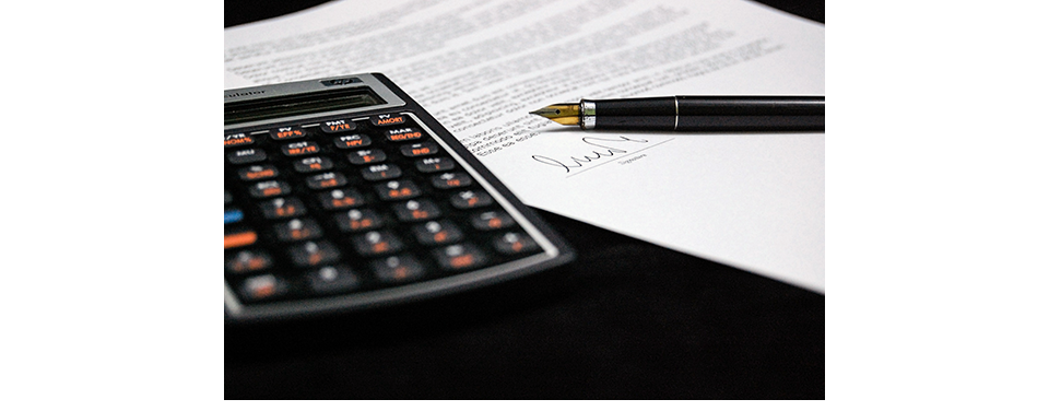 Calculadora, documentos y pluma fuente sobre una mesa.