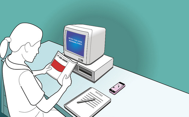 persona sentada frente a computadora, leyendo un manual de inducción impreso