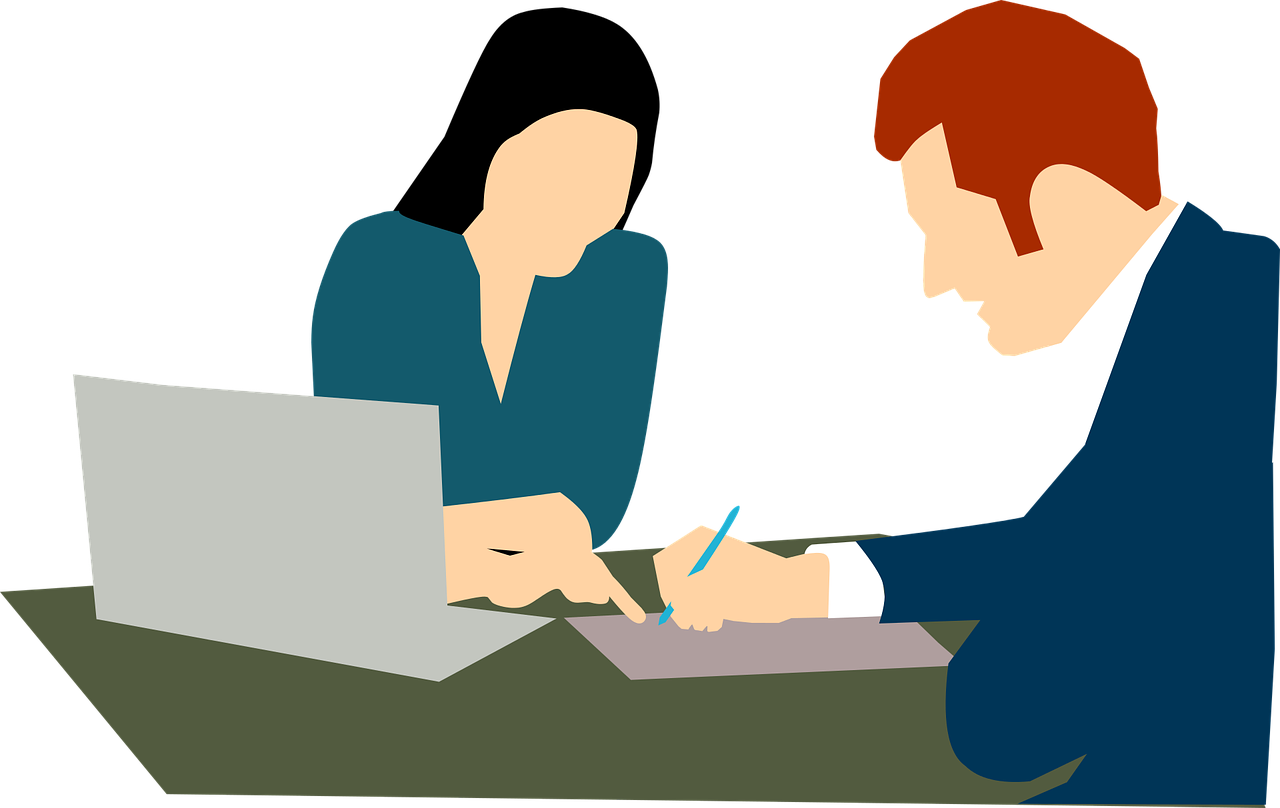 Imagen de dos personas revisando un documento, a un costado una computadora