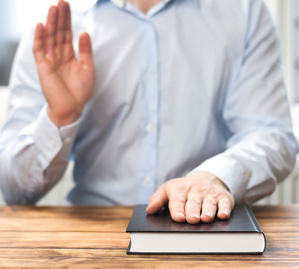 Persona con mano derecha alzada y la otra sobre libros.