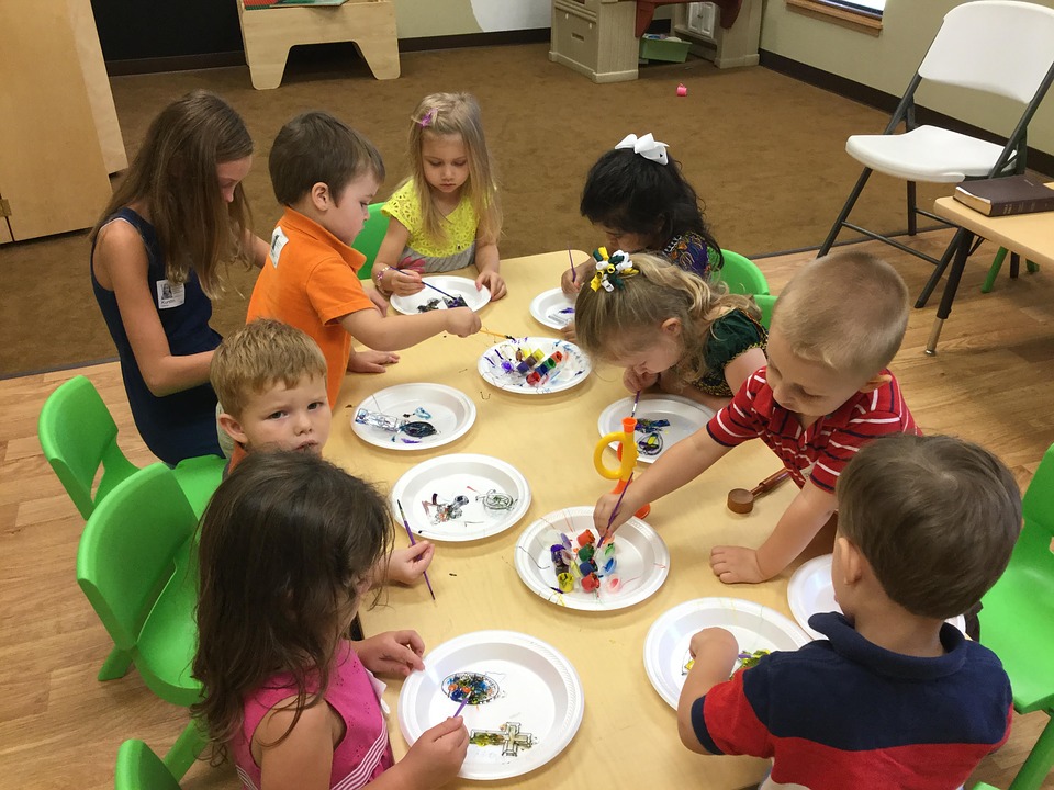 grupo de niños de edad preescolar en alrededor de una mesa pintando.