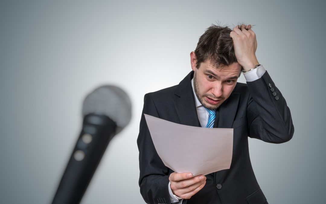Hombre preocupado (vestido de traje) quien sostiene y mira un papel. De lado izquierdo, se muestra un micrófono.