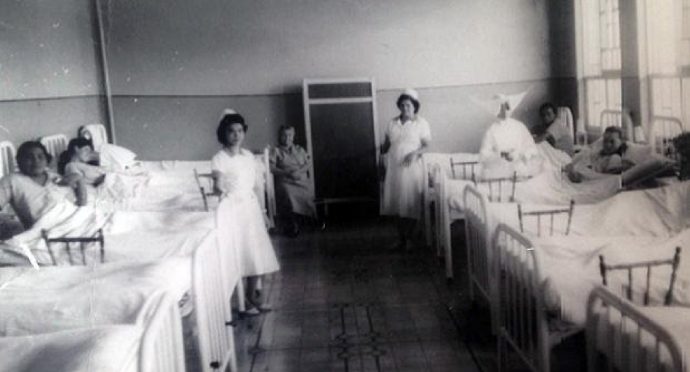 Cuarto con enfermos sobre camas y enfermeras de pie