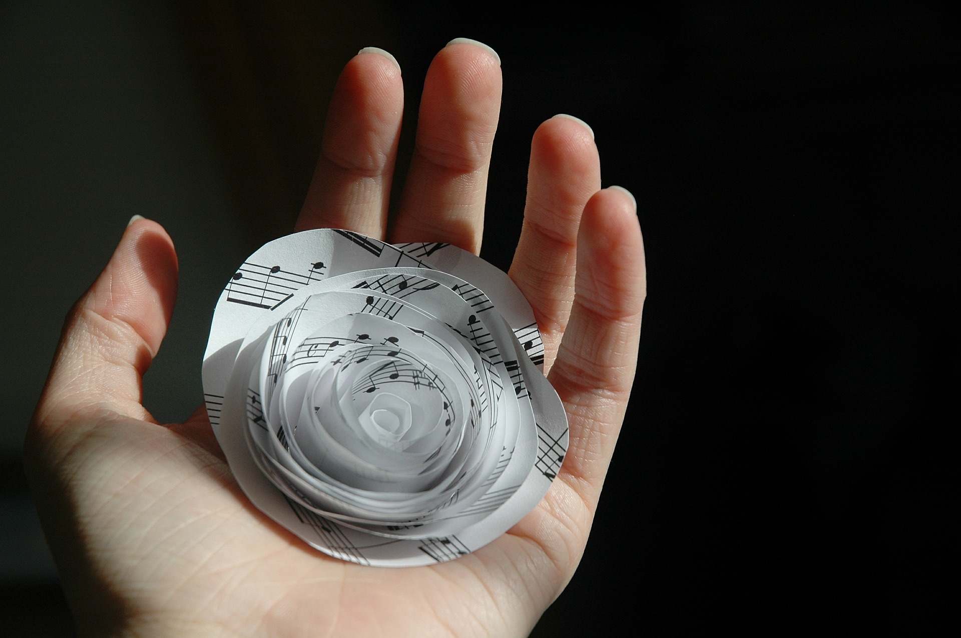 acercamiento a la palam de una mano que sostiene una rosa hecha con papel de una partitura.